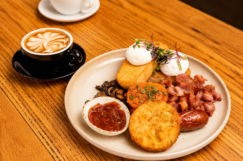 A big breakfast of poached eggs, bacon, sausage, hash brown, mushrooms and relish, with a coffee alongside