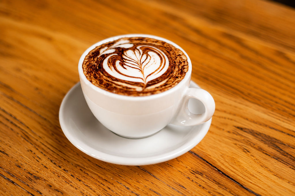 A cappuccino with latte art, in a white cup on a wooden table